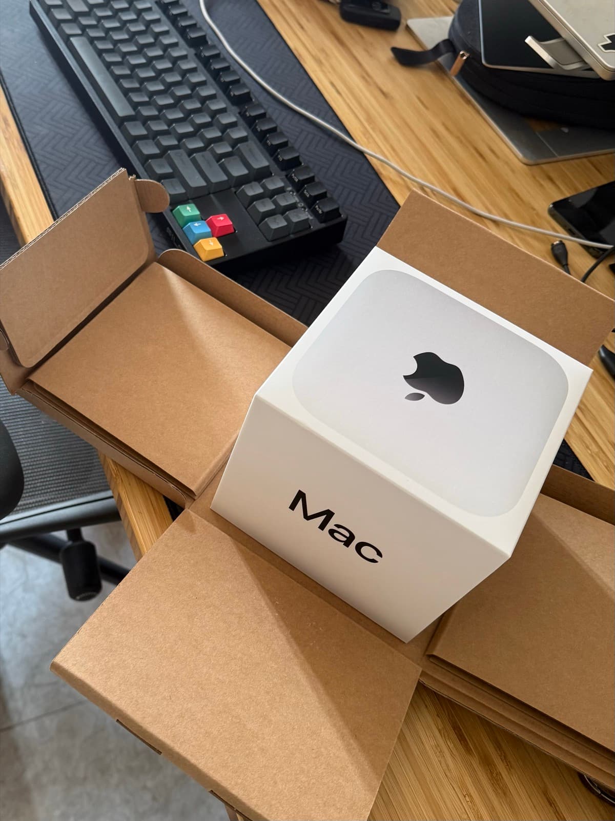 The Mac Mini still in its box, sitting on a desk next to a mechanical keyboard